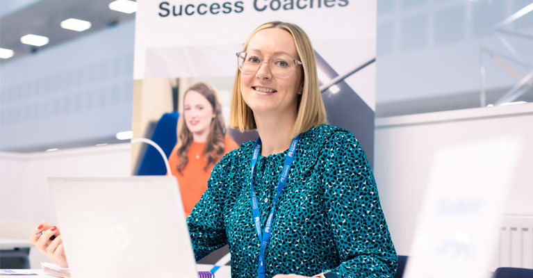 A success coach with an open laptop in front of her, smiling at the camera.