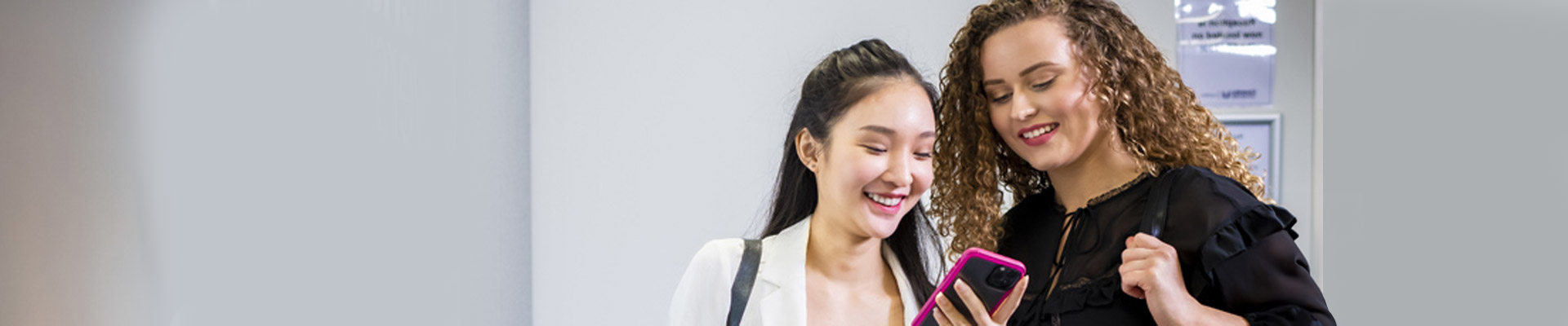 Two international students smiling at what is on one's mobile phone.