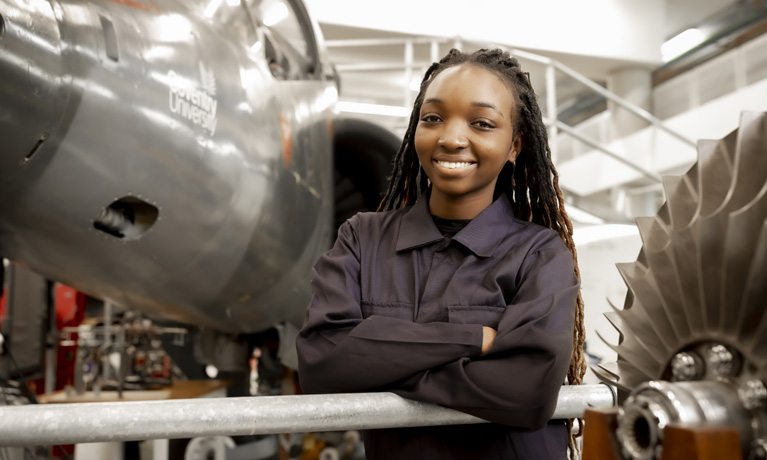 A BME female student in overalls stood in front of the Harrier jet in the Engineering building.