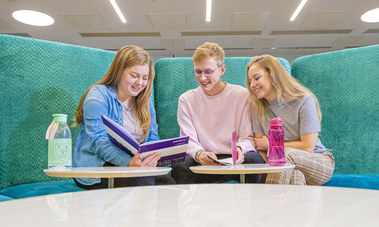 Three students sat looking at a leaflet