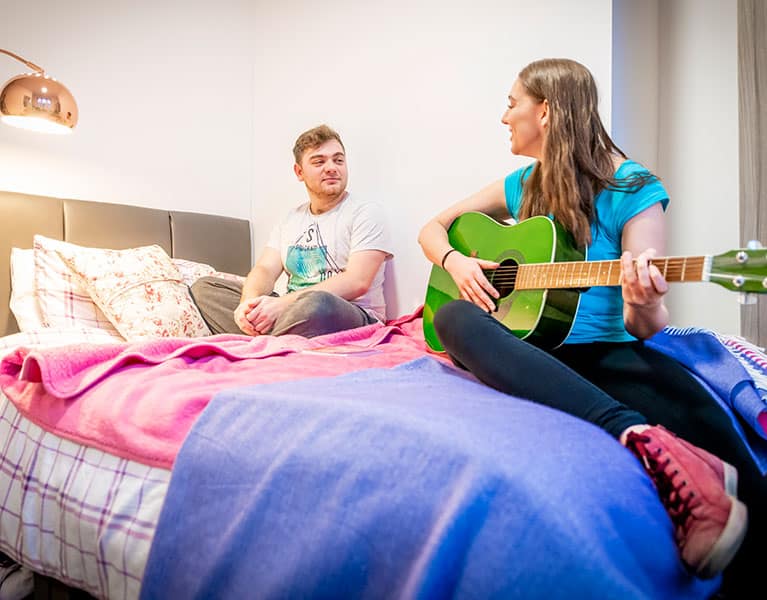 Students sitting on a bed playing a guitar