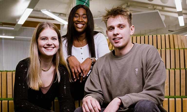 A group of three students sat down smiling at the camera