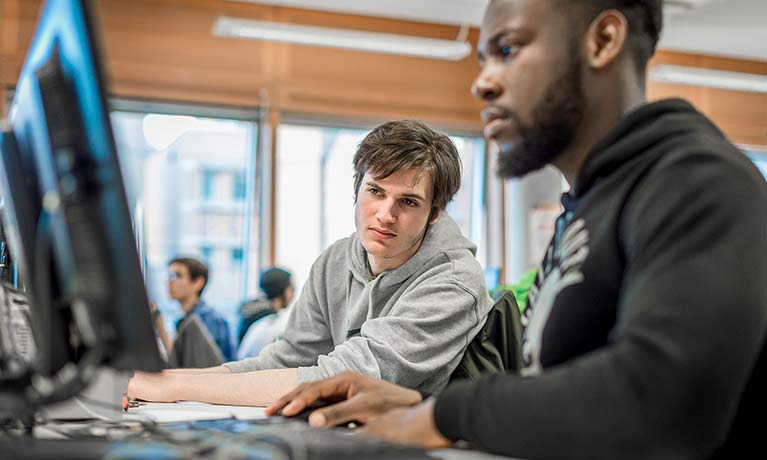 Two male students looking intently at a computer monitor.