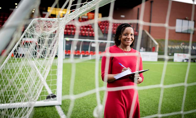 female sport manger holding a clipboard standing in football goals 