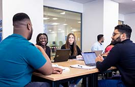 A group of students around a table smiling and talking. 