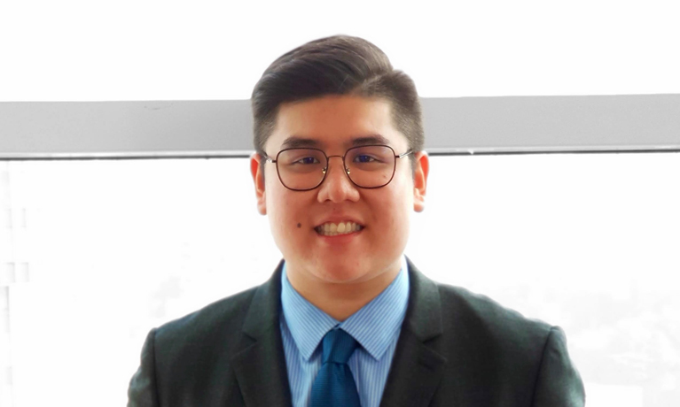 A headshot of Justin Tay in a suit and tie, smiling at the camera.