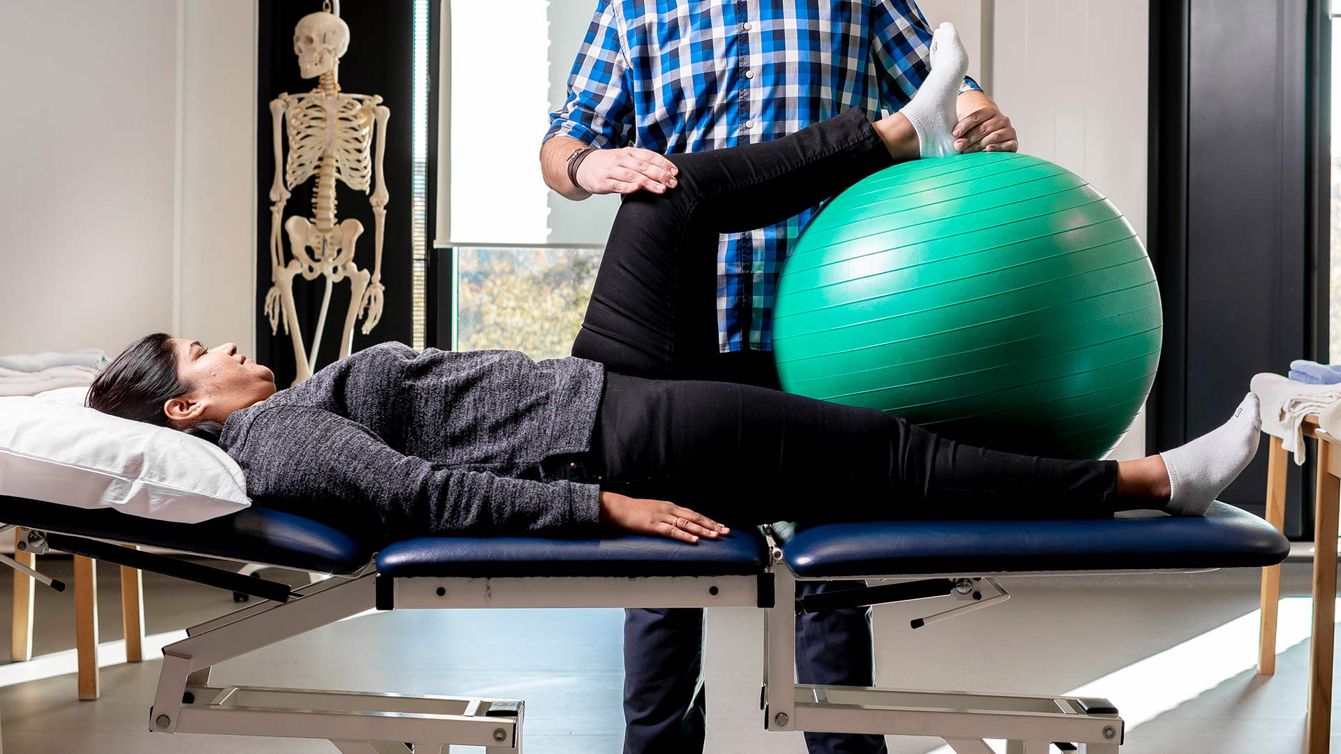 A patient lies on a treatment bed, large inflatable ball beside them and someone standing next to them