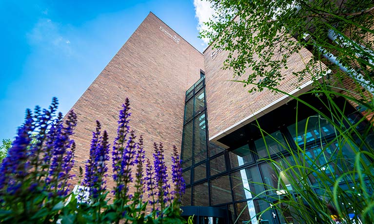 External view of the Alison Gingell Building with purple flowers in the grass outside.