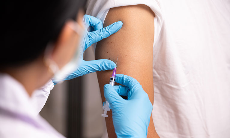 A nurse in scrubs placing an injection in someones arm