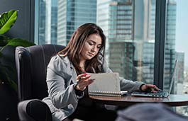 Female student in smart dress sitting at a desk looking at a notebook and laptop