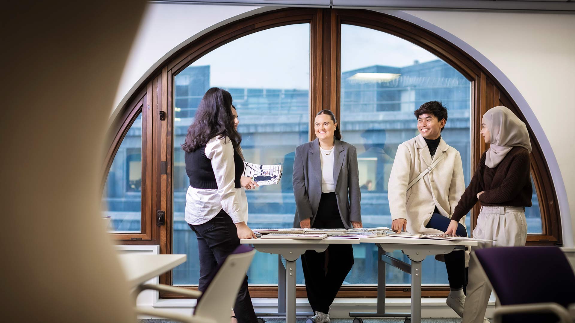 3 females and 1 male standing at table looking at a design 