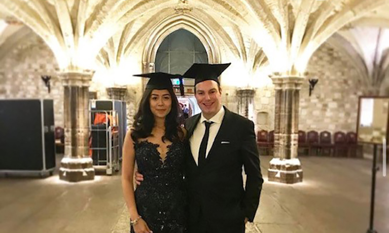 Robert at his graduation stood in a hall with a lit up background