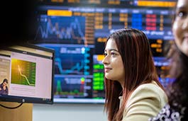 Adult female wearing a beige jacket looking at a monitor displaying a graph