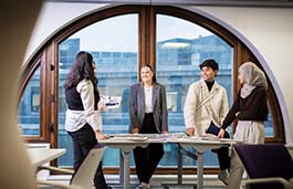 3 females and 1 male standing at table looking at a design 