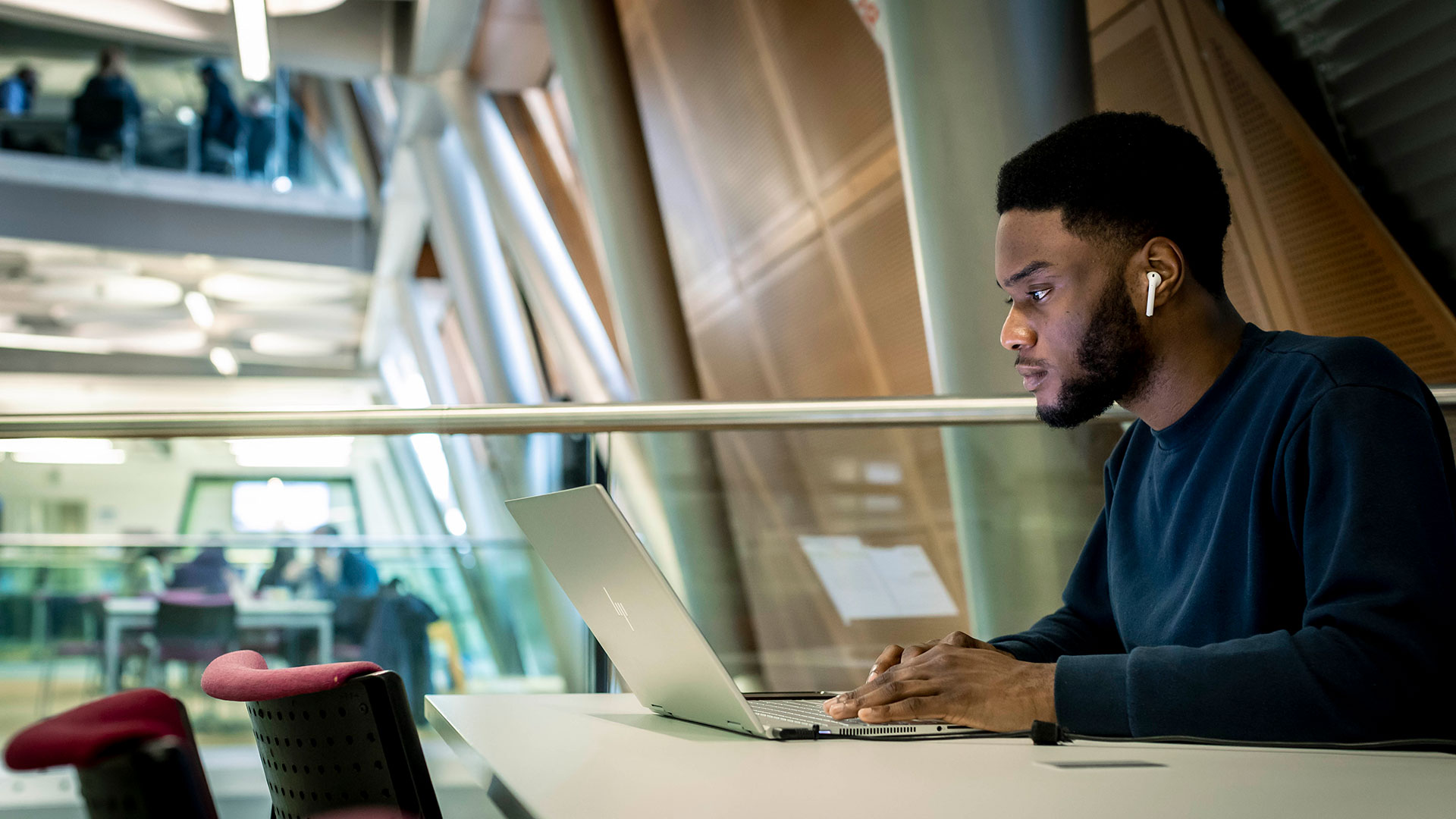 A student with earbuds in focuses intently on his laptop