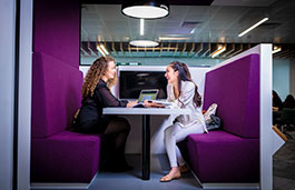 Two students sat round a table in a booth on campus talking to each other