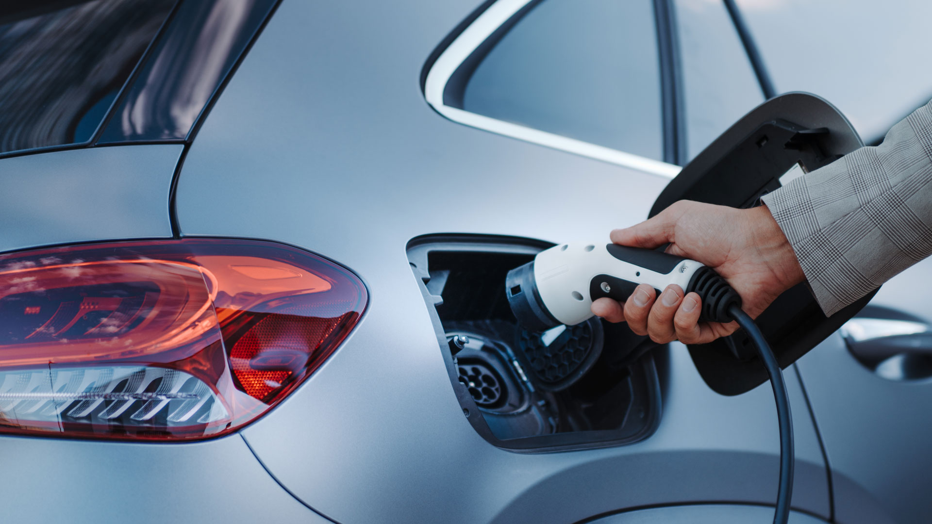 Hand holding an ev charger reaches to put it into a port on a car