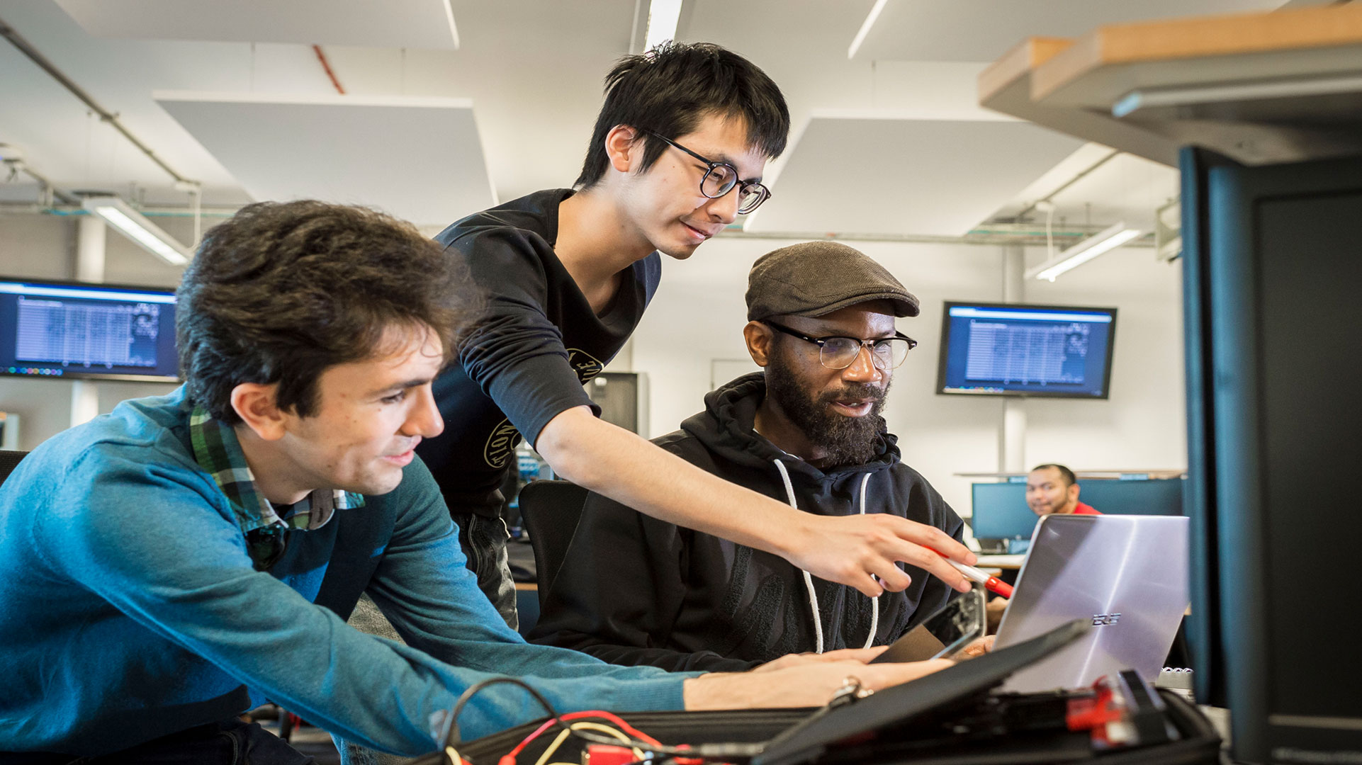 Three people lean over a screen, the middle one standing and pointing at the screen.