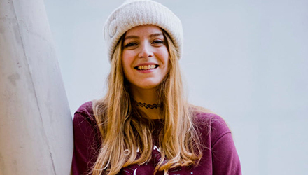 A student wearing a hat and jumper smiling towards the camera