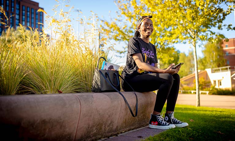 Female student sat on a wall outside on a sunny day