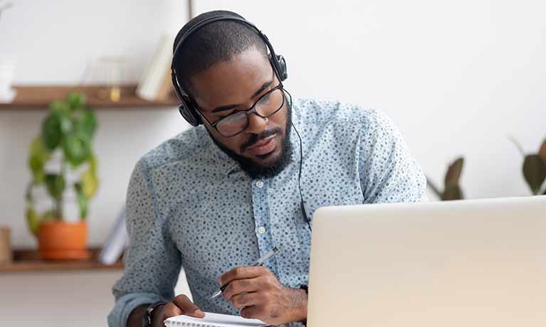 Male postgraduate student wearing headset looking at a laptop