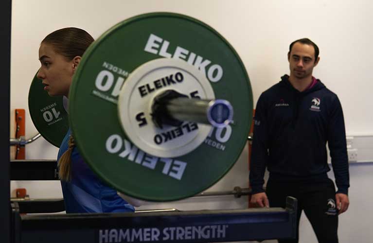 girl lifting weights being supervised by a male trainer