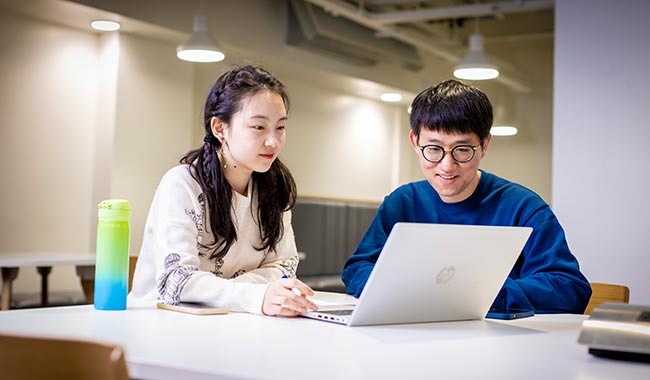 Two students sat at a table looking at a laptop