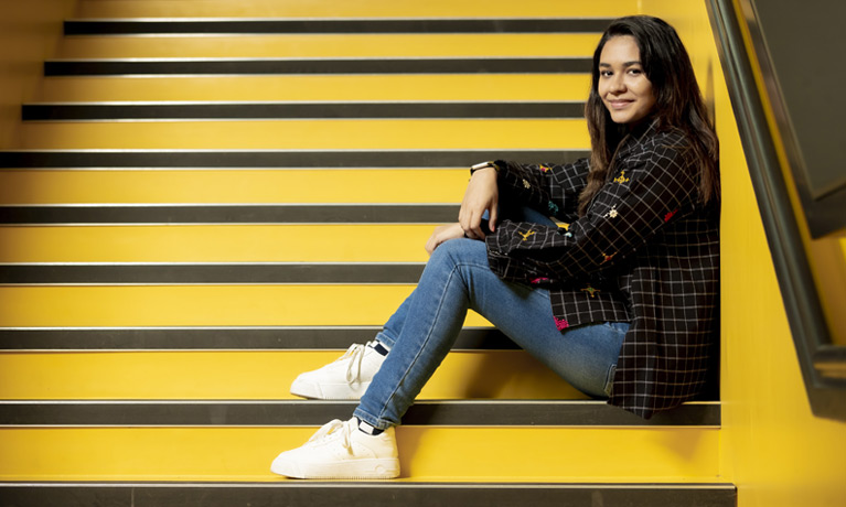 A female student sat on the steps of a campus building, smiling at the camera.