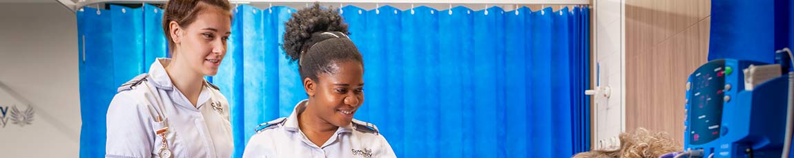 Two student nurses looking at patient laying in bed