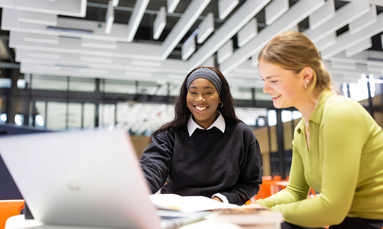 Two students sat inside a building working on a laptop