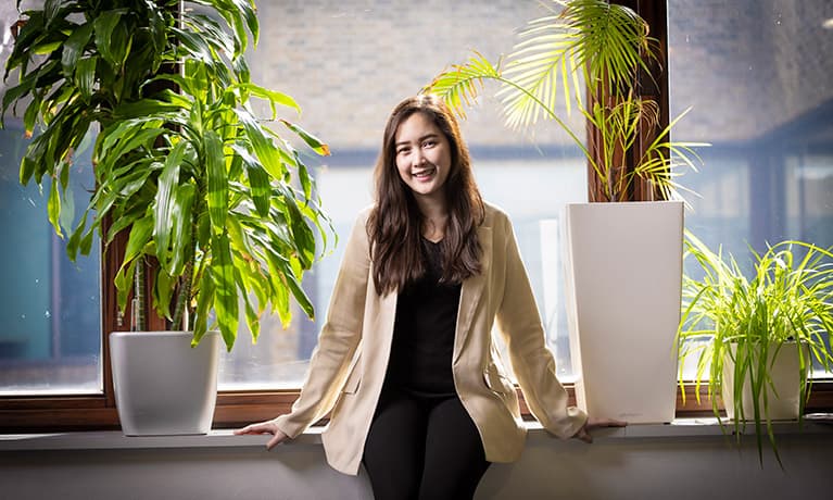 Female student leaning against a desk with green plants