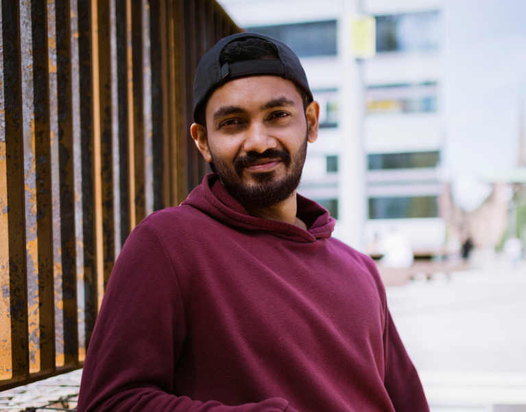 A make student leaning against a wall and smiling at the camera.