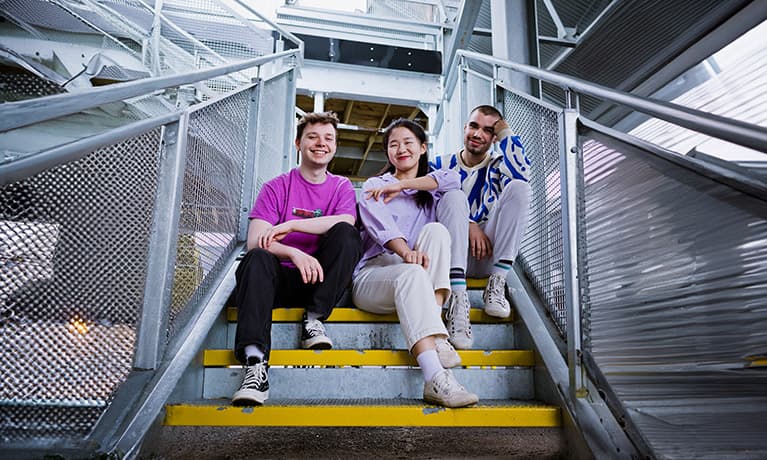 Three students sat on a staircase smiling