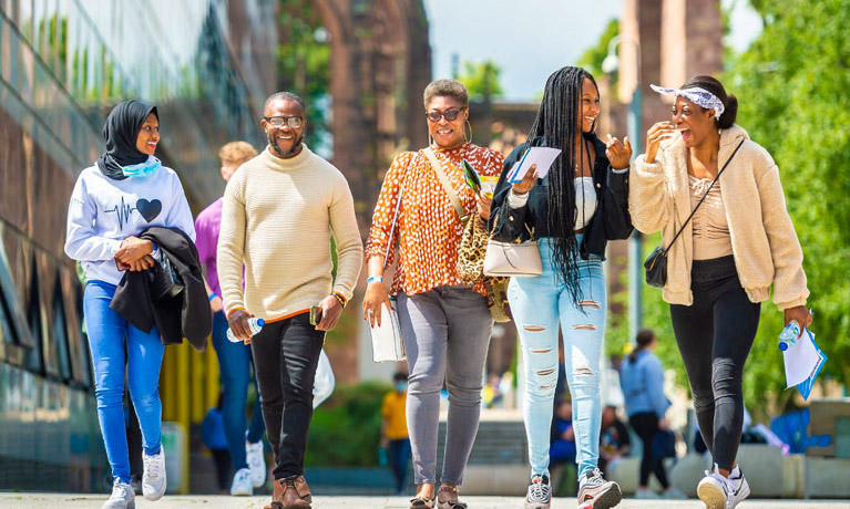 Students at an Open Day with family, walking past The Hub with Coventry Cathedral in the background.