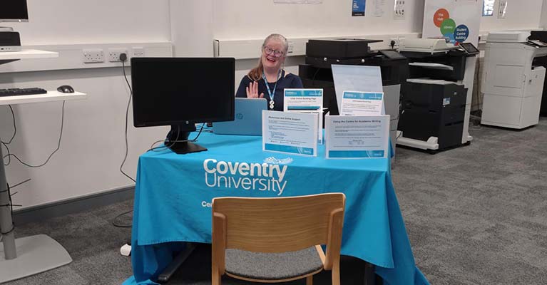 Academic writing tutor sat a table with leaflets on 