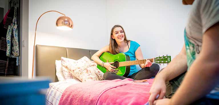 Student in bedroom playing a guitar in student accommodation