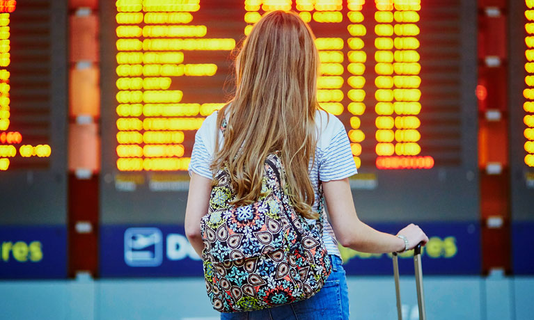 Woman wearing a backpack looking at airport flight times