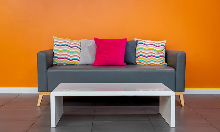 A grey sofa with colourful cushions against a bright orange painted wall