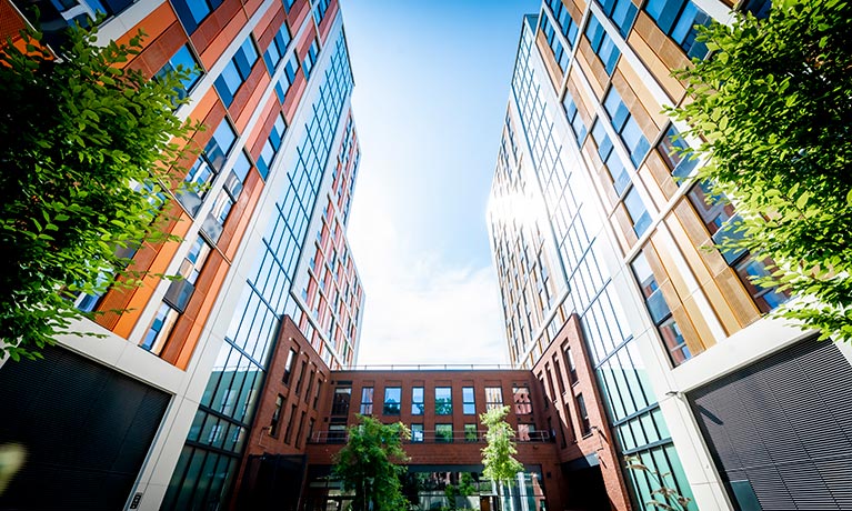 Outside view of a tall accommodation block with bright coloured cladding and trees.