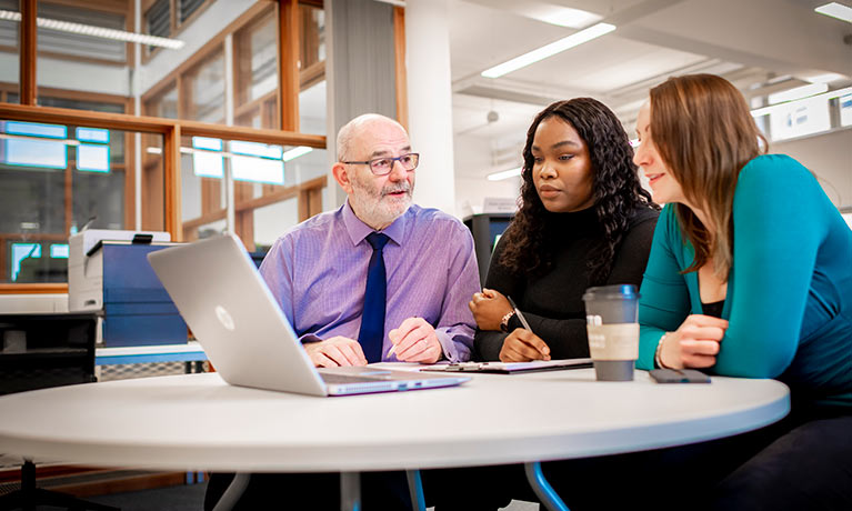 Two students sat with a tutor looking at a laptop screen.