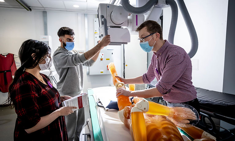 Radiography suite, a staff member helps a patient in a machine