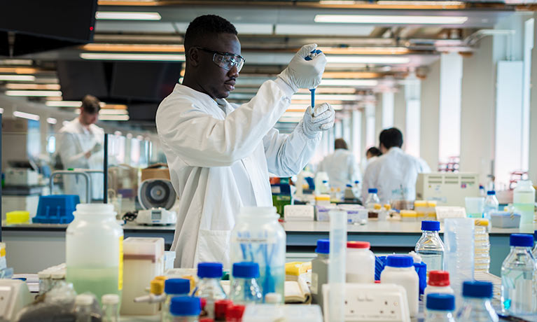 Student in white lab coat in the SuperLab using a syringe and test tube.