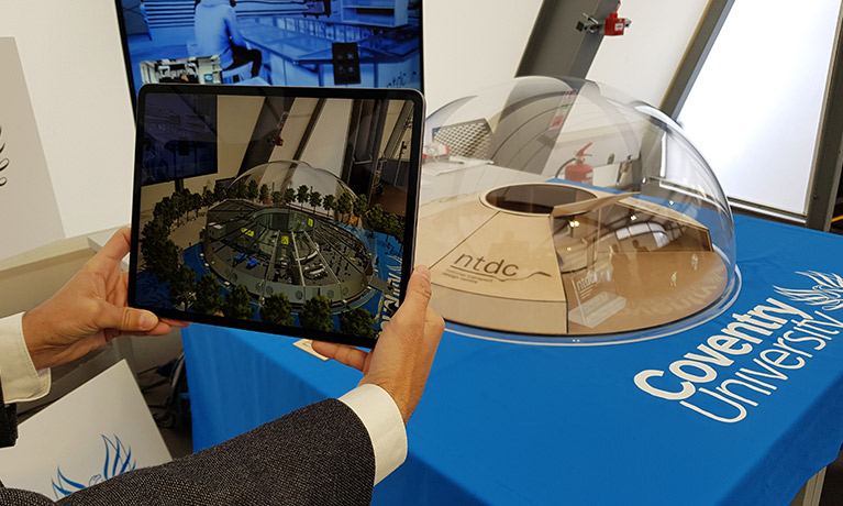 A man's hands hold up a tablet taking a photograph of a miniature model of an urban airport