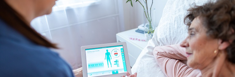 Female patient on bed shown information on tablet by nurse.