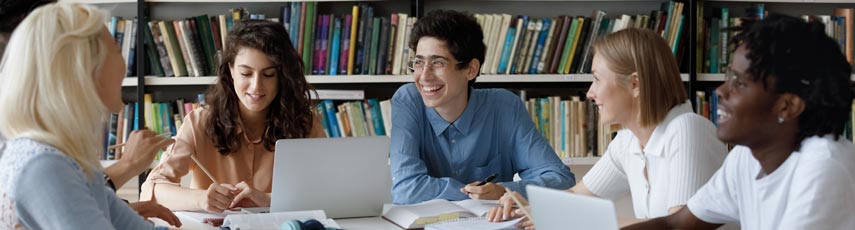 Students chatting around a desk in library.