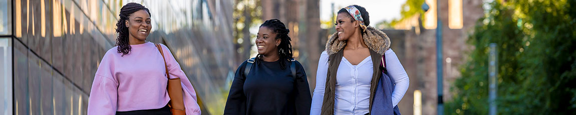 three female students walking past the side of the Hub talking