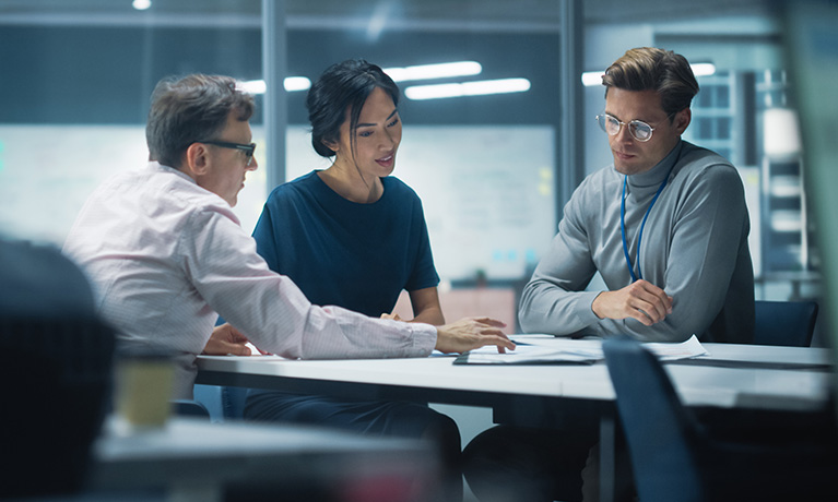 Two men and a woman in business wear having a discussion around a table in modern office.