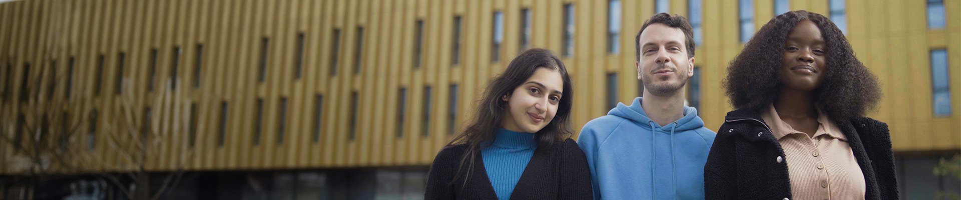 Three ethnically diverse students stood in front of Coventry University's Delia Derbyshire building.