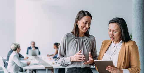 2 females chatting whilst looking at a tablet in a conference room