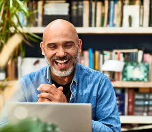 Bald smiling male clasping his hands looking at a laptop screen sitting in a home office 